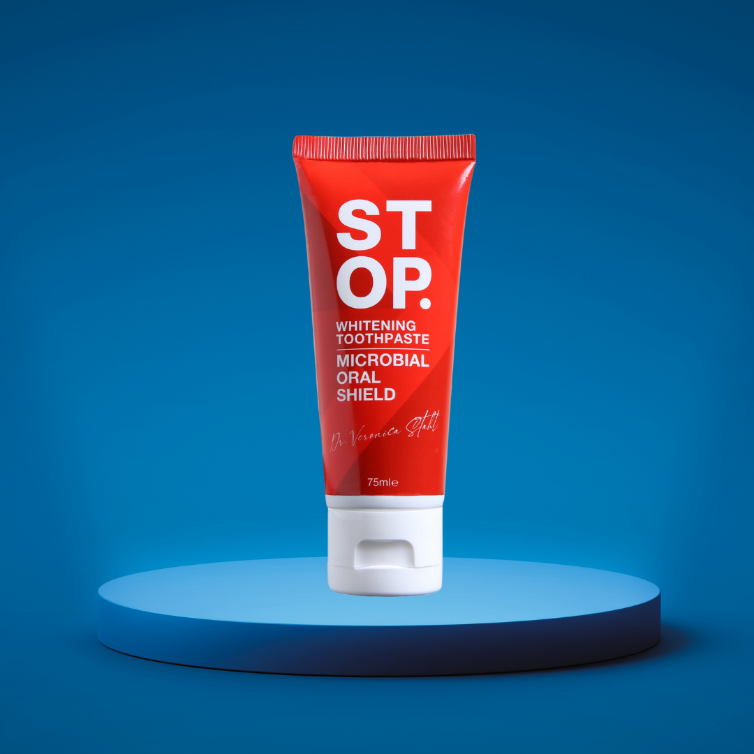 Red 'STOP' whitening toothpaste tube highlighting 'Microbial Oral Shield' feature, signed by Dr. Veronica Stahl, standing upright on a lighted blue platform against a deep blue backdrop.