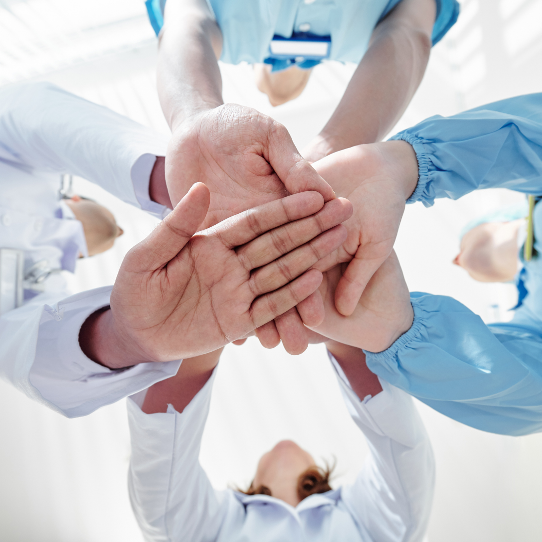 Close-up of medical professionals stacking hands in unity, symbolizing teamwork and collaboration in a clinical setting.